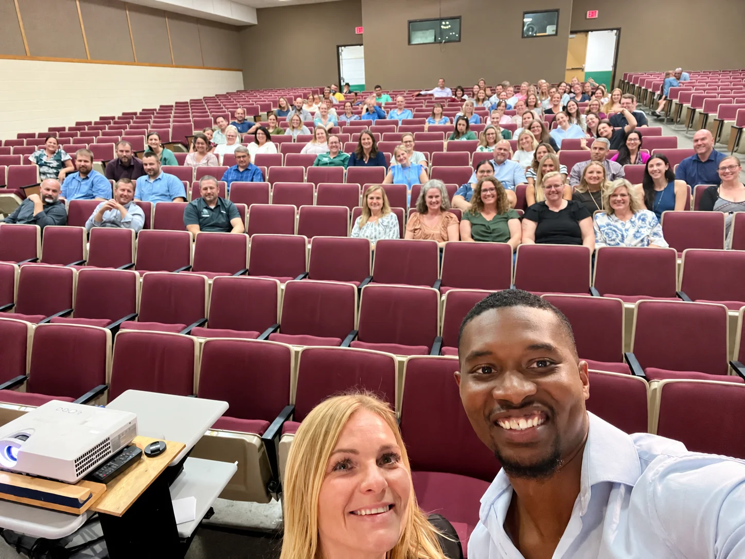 Lacey Cook and Iván Quintero in front of Elk Lake School District faculty and staff seated in an auditorium